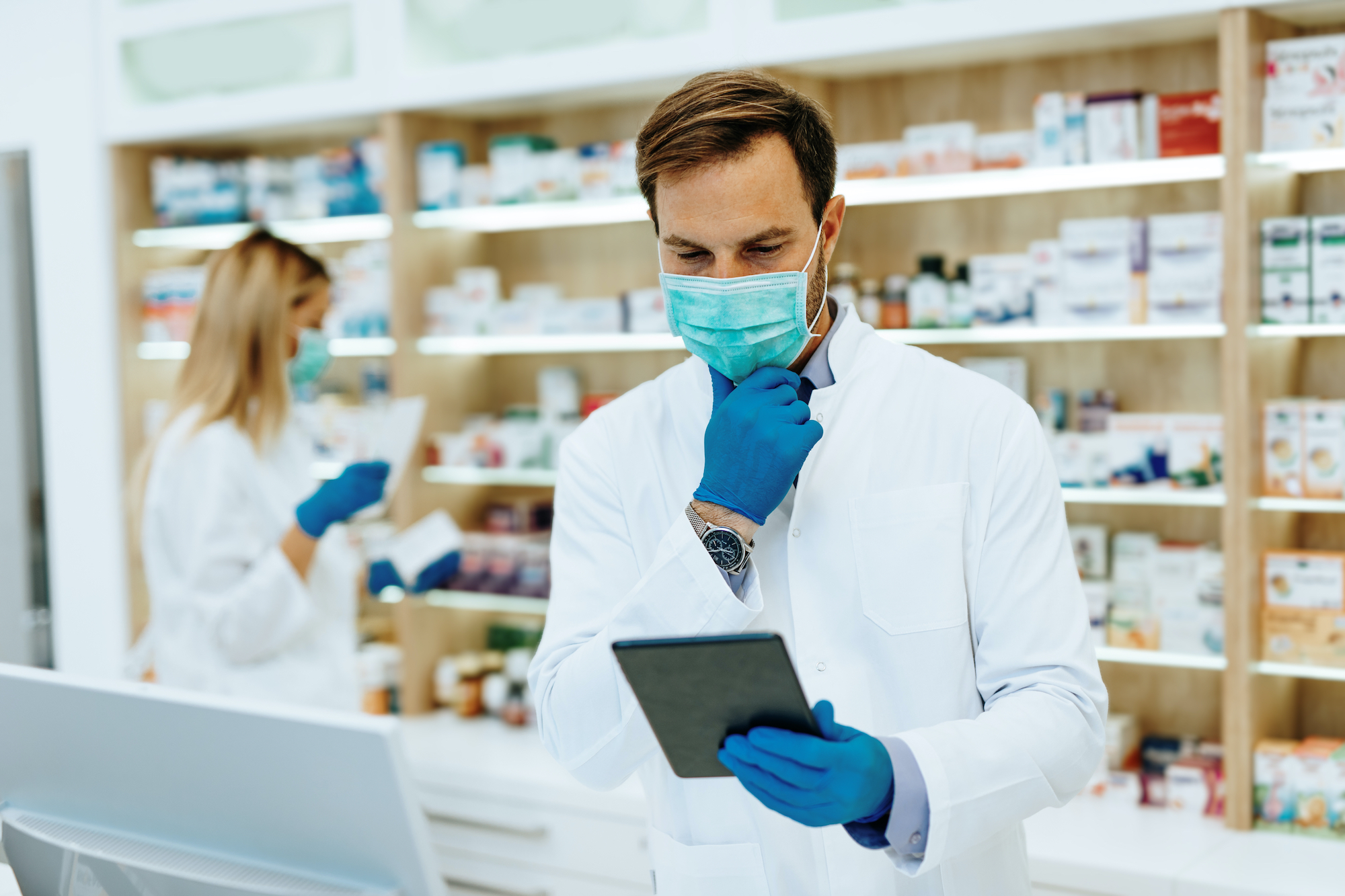Apotheker und Apothekerin mit Mundnasenschutz suchen Arzneimittel für Kunden heraus